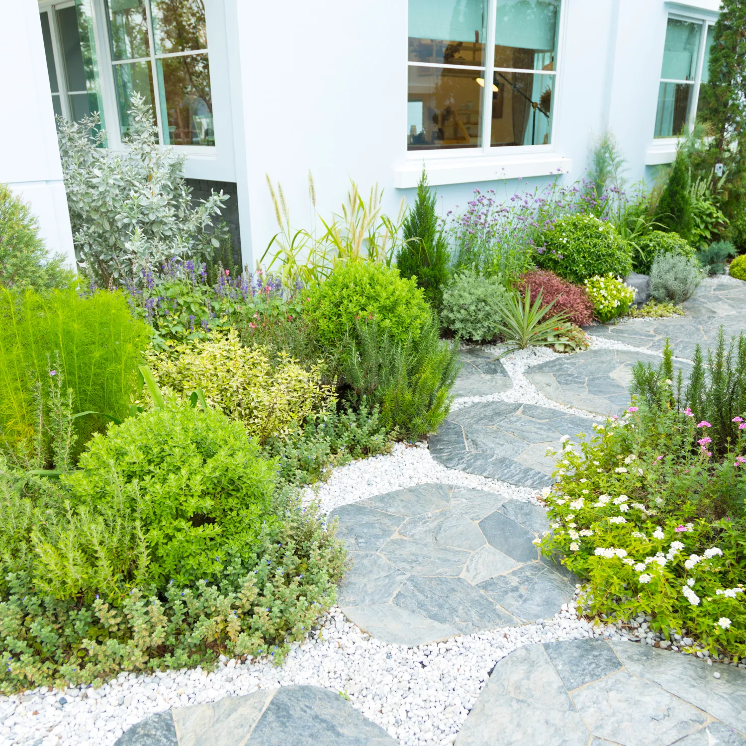 path with garden stones and gravel in front of a summery home with a beautiful manicured garden