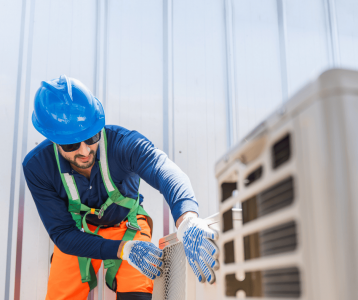 HVAC technician in safety gear inspecting outdoor unit to maintain efficient heating and cooling performance.