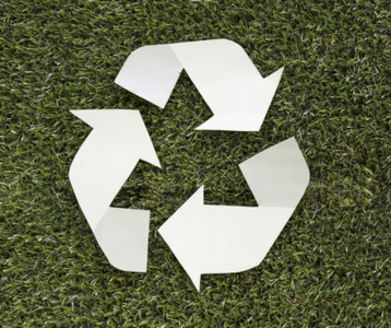 White recycling symbol on green grass representing sustainable waste reduction and eco‑friendly home habits.