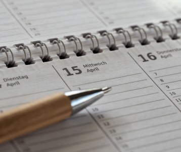 Open spiral planner showing mid‑April dates with pen resting on page for home maintenance scheduling.